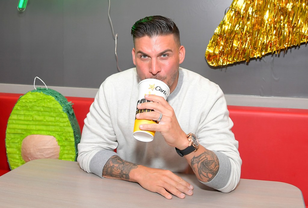 Jax Taylor sitting at a restaurant, wearing a grey sweater, and drinking out of a large soda cup