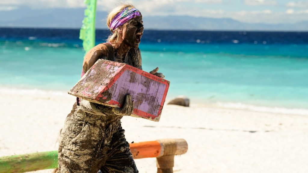 Carolyn Wiger carrying a box, covered in mud, and screaming on Survivor 44
