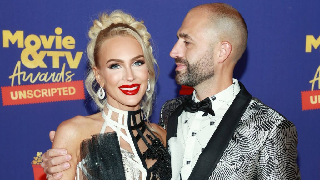 Christian Richard and Christine Quinn on a red carpet; Christian has his head turned to the side and is staring at Christine