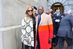 Gizelle Bryant in a black and white coat posing with Pastor Jamal Bryant waring a red coat; military officials are in the background
