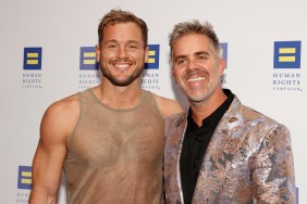 Colton Underwood in a sheer tank top posing with husband Jordan C. Brown who is wearing a multicolored blazer