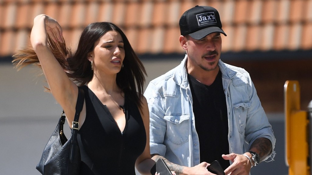 Jax Taylor and Paige Woolen walking together; she's wearing all black and has her arm in the air; he's wearing a denim jacket and a black hat