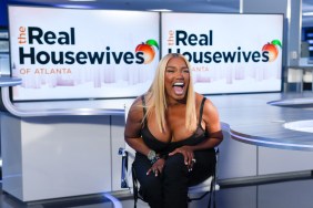 NeNe Leakes laughing with her mouth wide open, sitting in front of two televisions displaying the Real Housewives of Atlanta logo