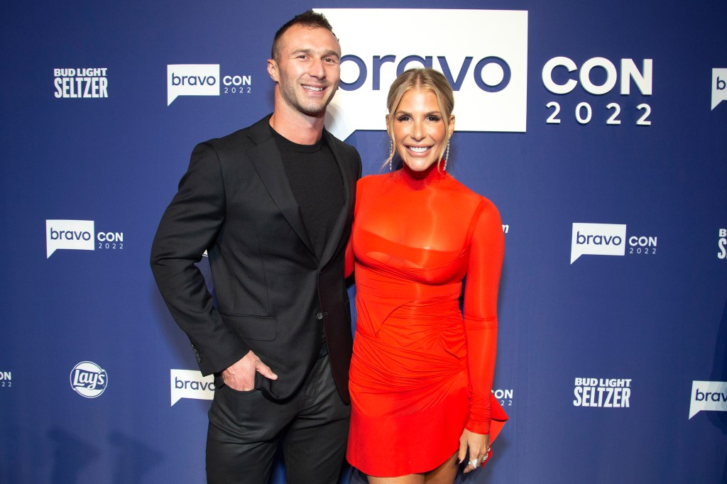 Tracy Tutor in a red dress posing with Erik Anderson in a black suit at BravoCon 2022