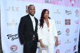Oliver Saunders in a black suit posing with Garcelle Beuvais, who is wearing a white suit