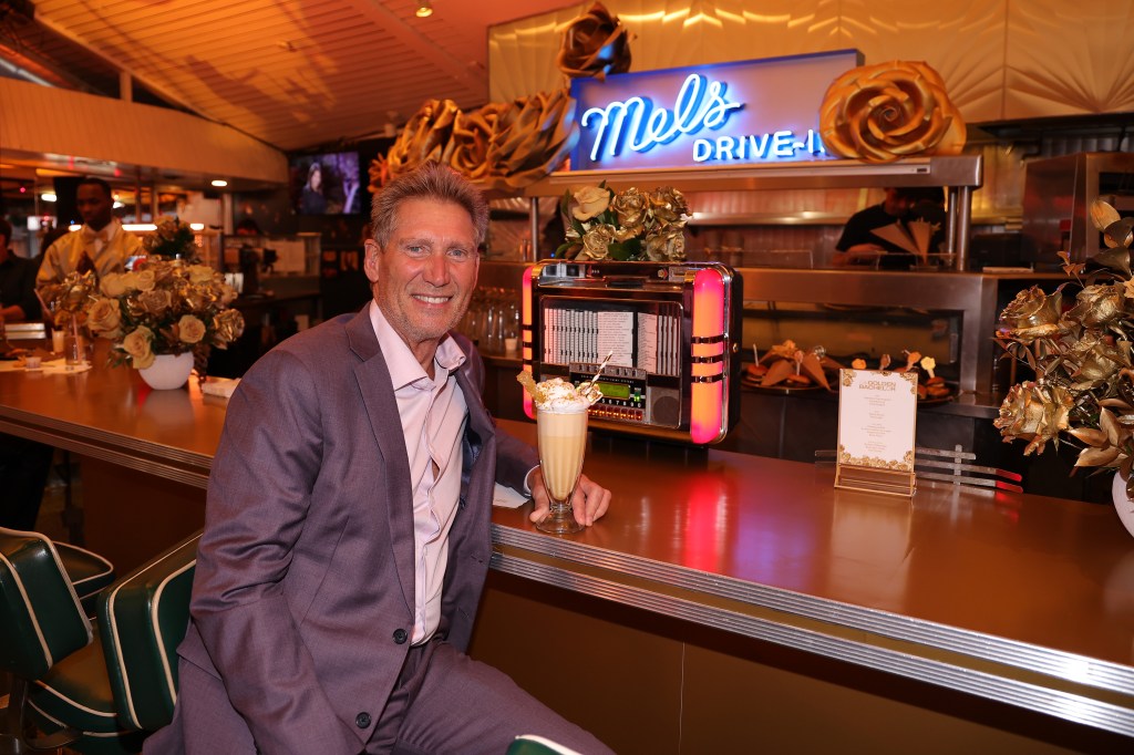 Gerry Turner in a grey suit sitting at a counter in a restaurant with a milkshake