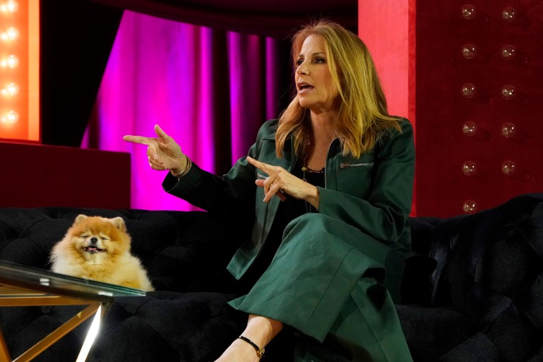 Jill Zarin and her dog sitting on a couch at BravoCon 2022; Jill is pointing and wearing a green suit
