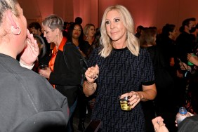 Vicki Gunvalson in a sea of people, smiling, wearing a black dress, and holding a cocktail
