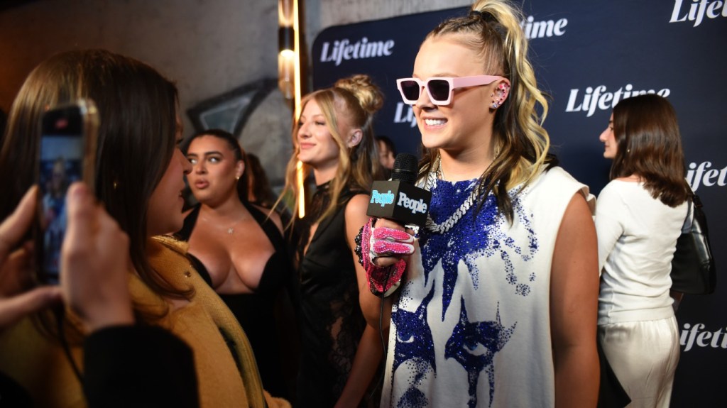 JoJo Siwa speaking into a microphone during a red carpet interview