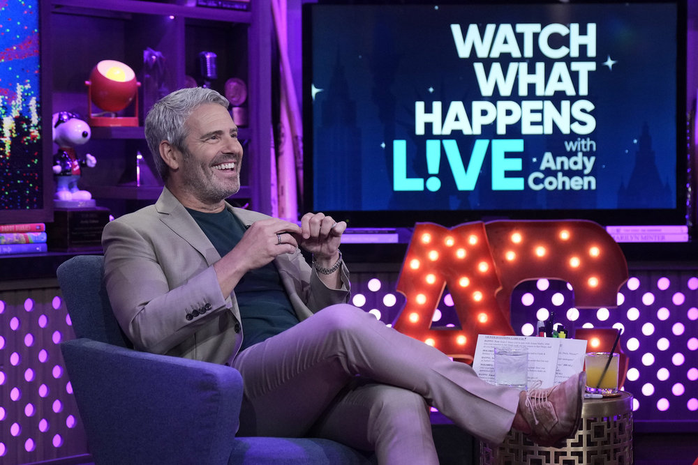 Andy Cohen sin a grey suit sitting with his legs crossed on Watch What Happens Live