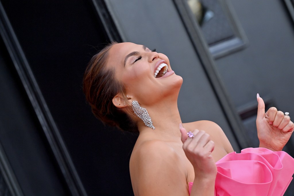 Chrissy Teigen happy about something in a pink dress. 