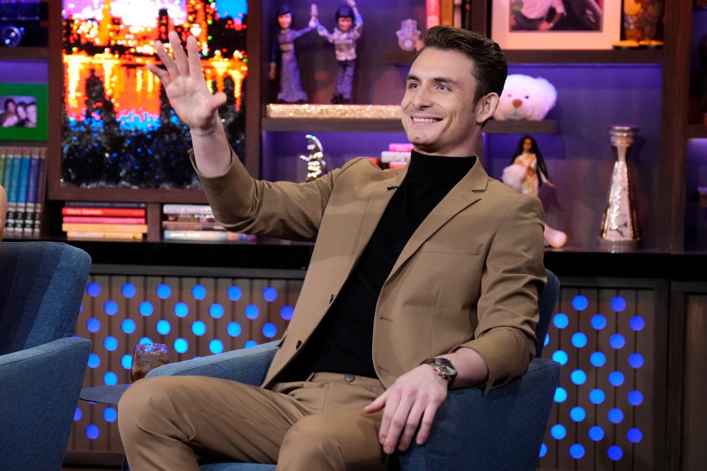 James Kennedy in a brown suit with his right hand in the air on WWHL.