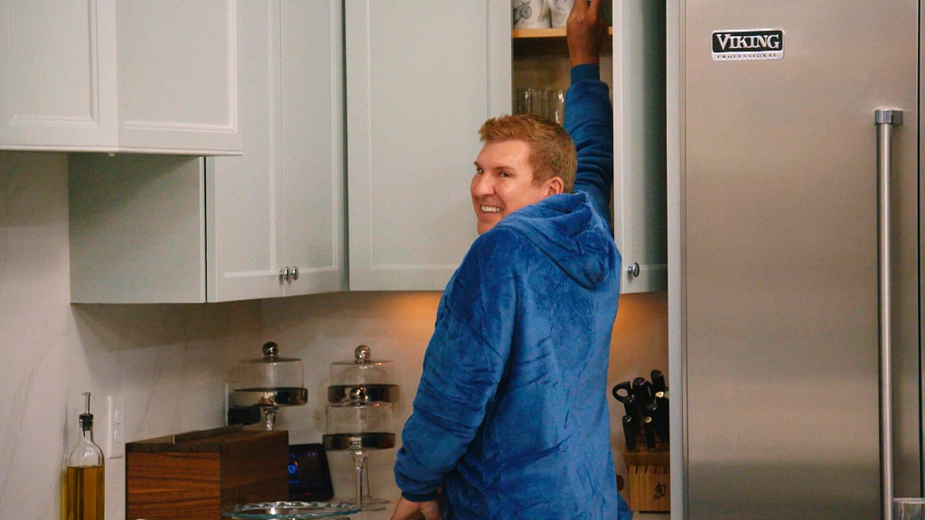 Todd Chrisley in a blue robe looking back at he reaches into a cabinet