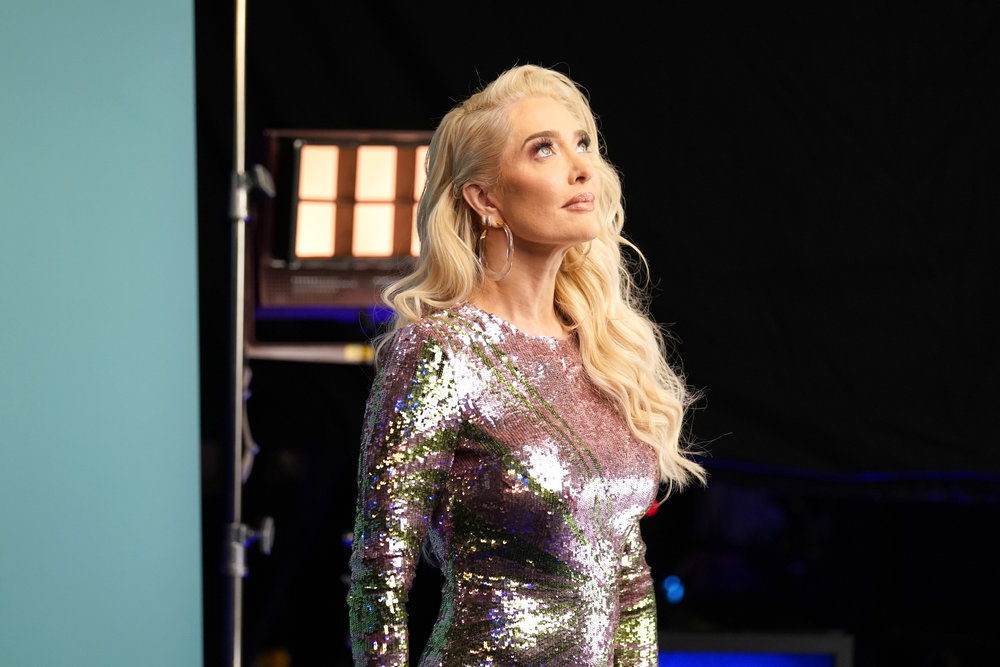 Erika Jayne in a silver dress looking upwards at the light