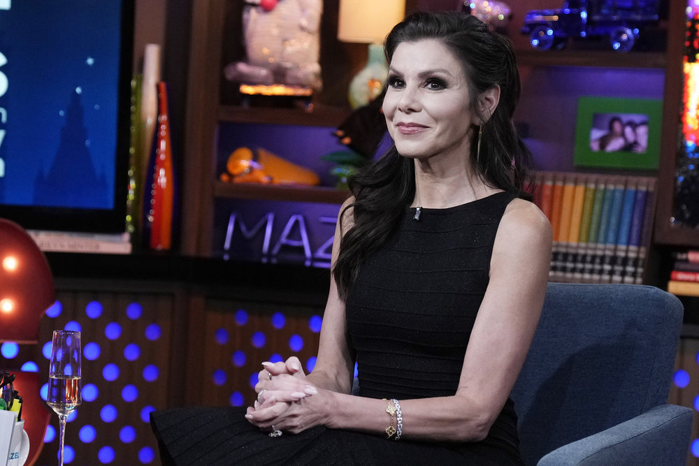 Heather Dubrow in a black dress sitting on Watch What Happens Live with her hands folded in her lap 