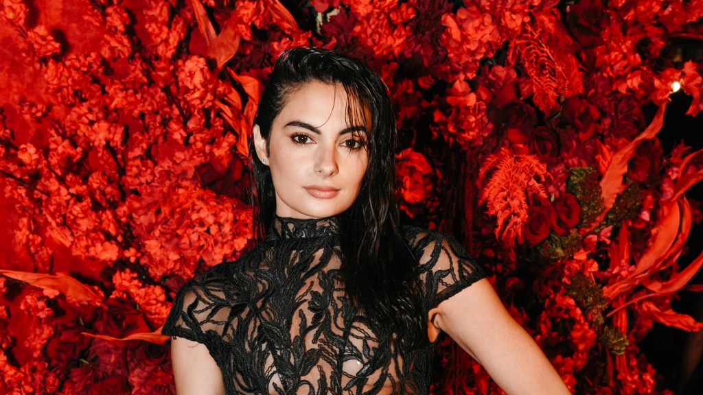 Paige DeSorbo in a black dress posing in front of red flowers